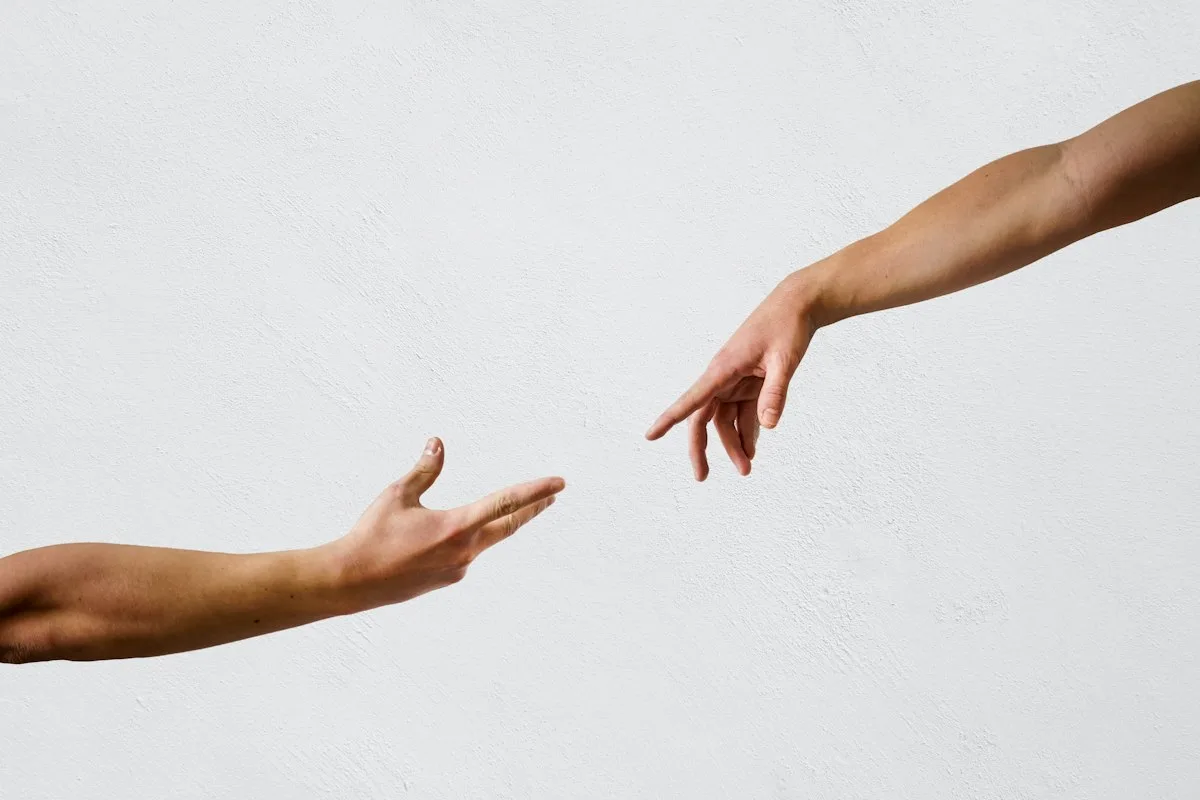 Two hands reaching toward each other without quite touching.