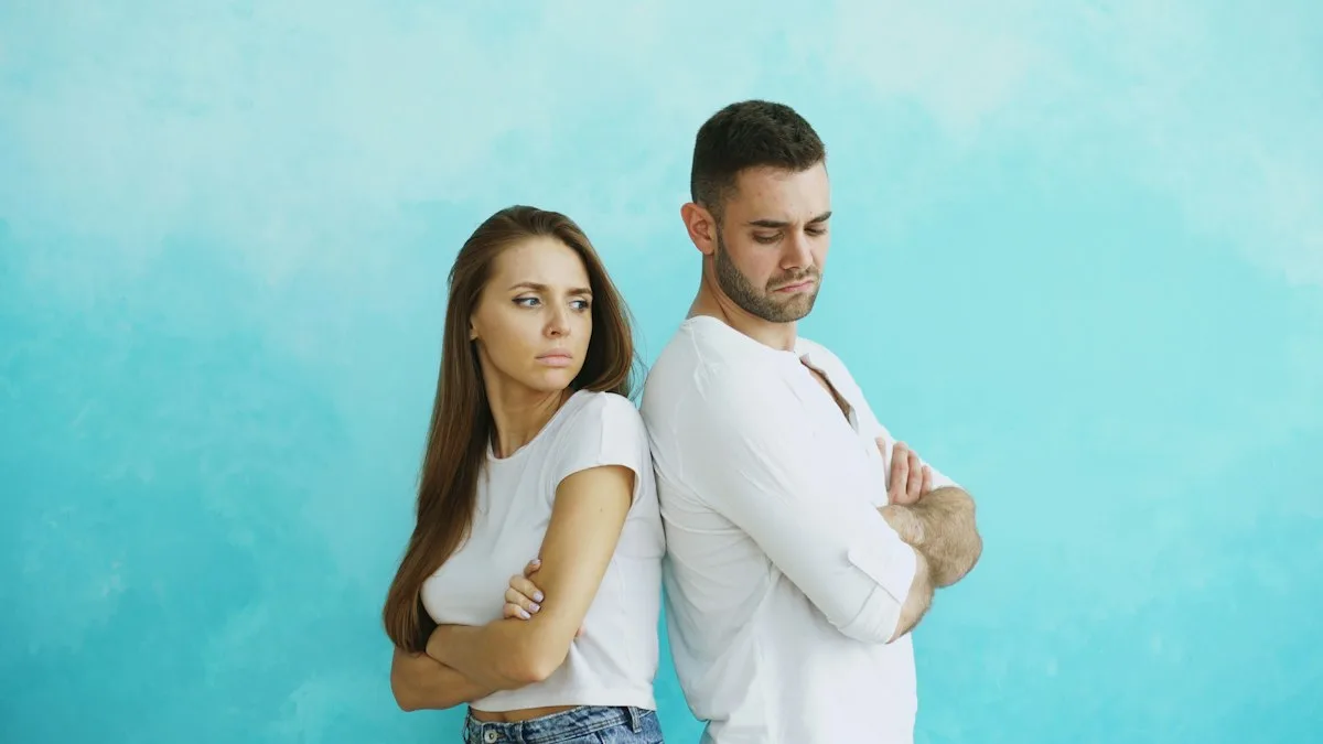 A couple standing back to back with arms crossed.