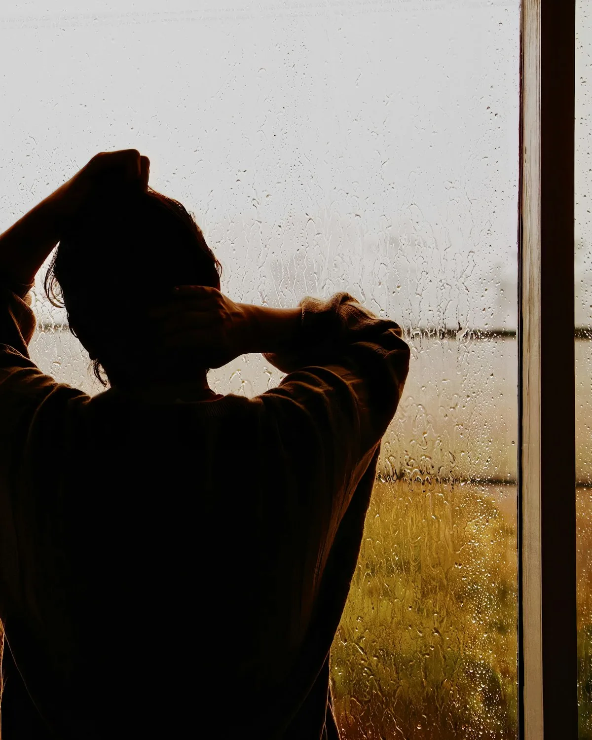 Someone standing in front of a rain-covered window.